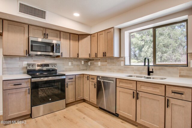 kitchen with stainless steel appliances, light countertops, visible vents, a sink, and light wood-type flooring