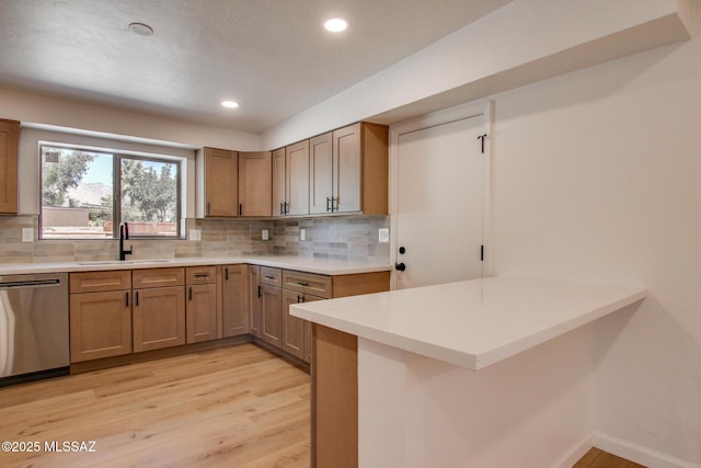 kitchen with a peninsula, a sink, light wood-type flooring, decorative backsplash, and dishwasher