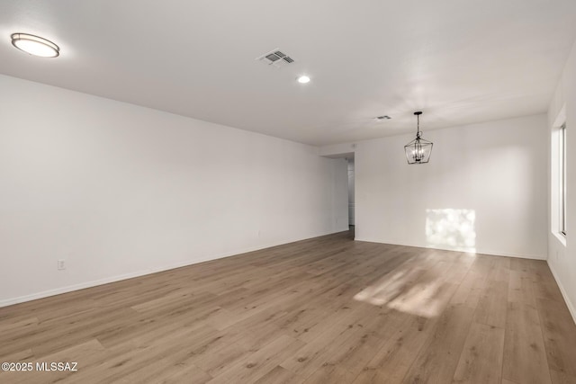 spare room featuring an inviting chandelier and light hardwood / wood-style flooring