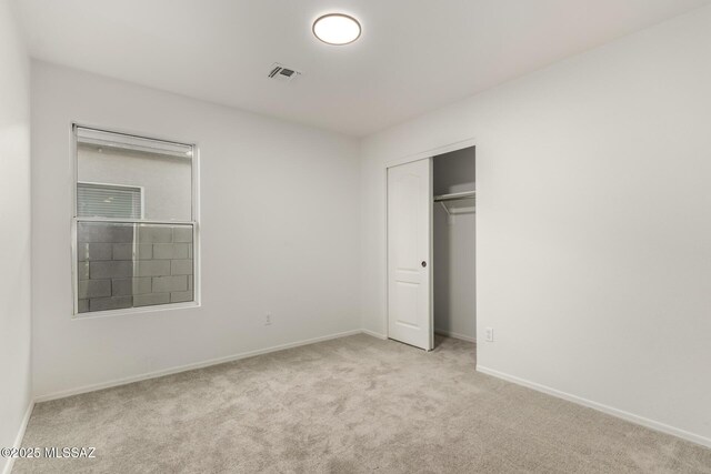 unfurnished bedroom with light colored carpet and a closet