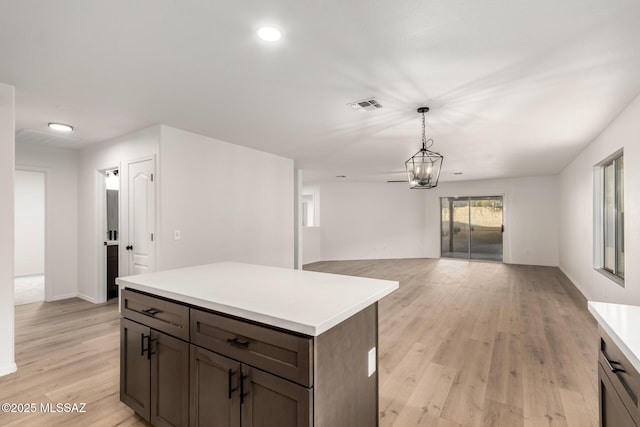 kitchen featuring dark brown cabinets, hanging light fixtures, a kitchen island, a notable chandelier, and light hardwood / wood-style floors