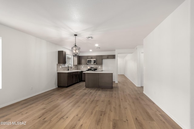 kitchen with tasteful backsplash, hanging light fixtures, light hardwood / wood-style flooring, a kitchen island, and stainless steel appliances