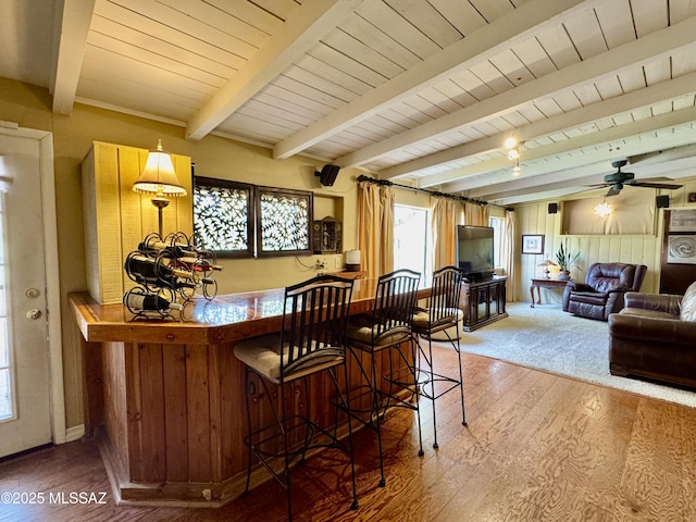bar featuring ceiling fan, a dry bar, wood walls, beam ceiling, and wood finished floors