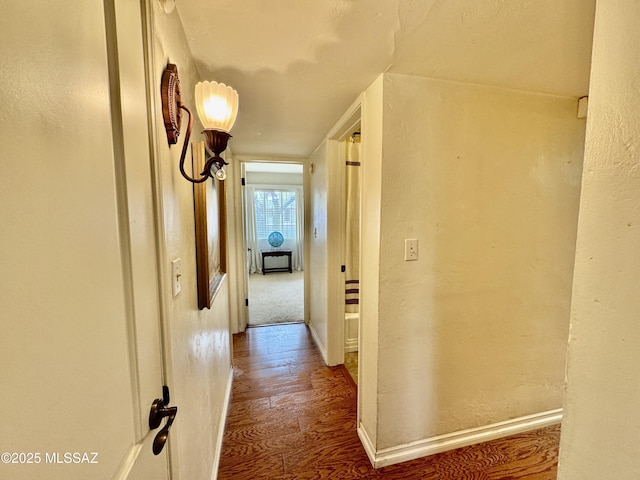 hall featuring a textured wall, wood finished floors, and baseboards