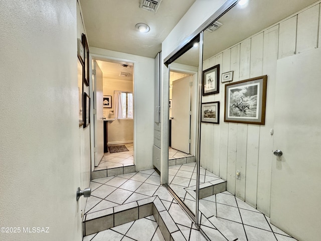 hallway with wood walls, light tile patterned flooring, and visible vents