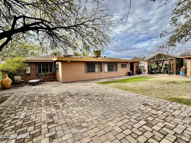 rear view of house featuring brick siding, a gazebo, a lawn, stucco siding, and a patio area