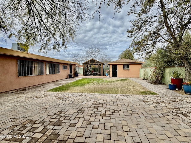 back of house featuring a gazebo, an outdoor structure, fence, and stucco siding