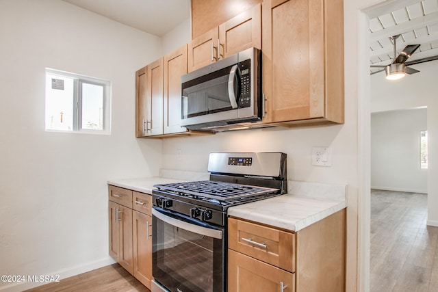 kitchen with appliances with stainless steel finishes, light brown cabinets, ceiling fan, and light hardwood / wood-style flooring