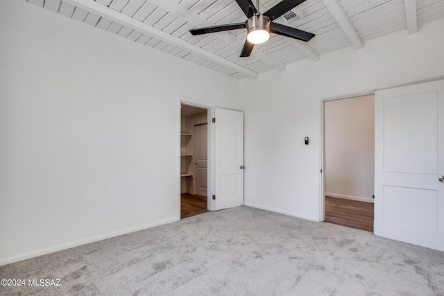 unfurnished bedroom with a spacious closet, wooden ceiling, ceiling fan, beamed ceiling, and light colored carpet