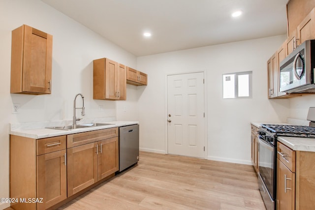 kitchen with appliances with stainless steel finishes, sink, and light hardwood / wood-style floors