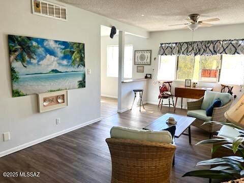 living room featuring dark wood-type flooring, ceiling fan, and a textured ceiling