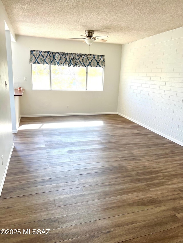 unfurnished room featuring brick wall, dark wood-type flooring, a textured ceiling, and ceiling fan