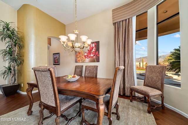 dining area with a notable chandelier, baseboards, arched walkways, and wood finished floors