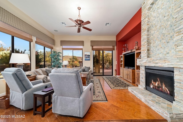 living area with ceiling fan, visible vents, a fireplace, and wood finished floors