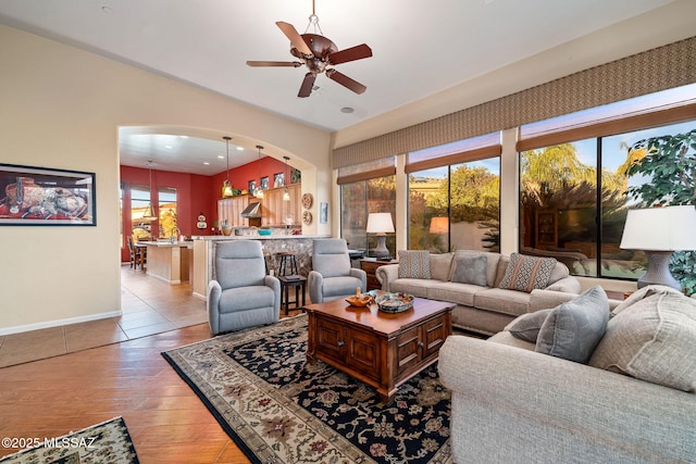 living room featuring arched walkways, ceiling fan, light wood-style flooring, and baseboards