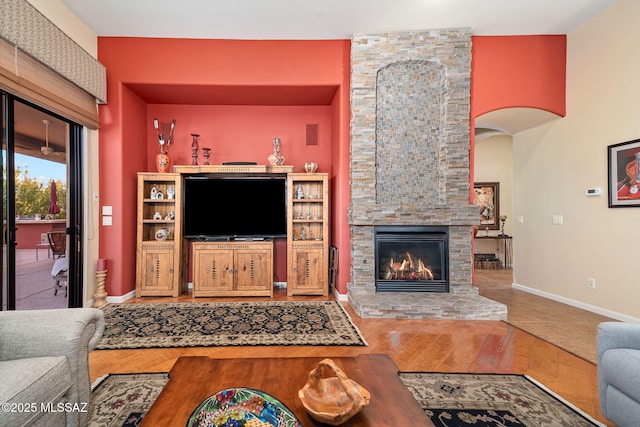 living area featuring baseboards, arched walkways, wood finished floors, and a stone fireplace