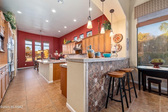 kitchen with pendant lighting, a center island with sink, visible vents, light tile patterned flooring, and wall chimney range hood