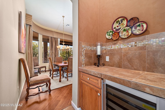 bar with a chandelier, wine cooler, visible vents, baseboards, and light wood-style floors