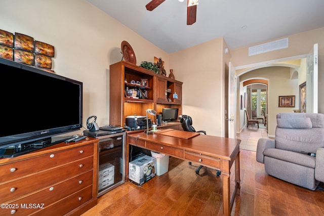 home office with light wood-style flooring, visible vents, arched walkways, and a ceiling fan