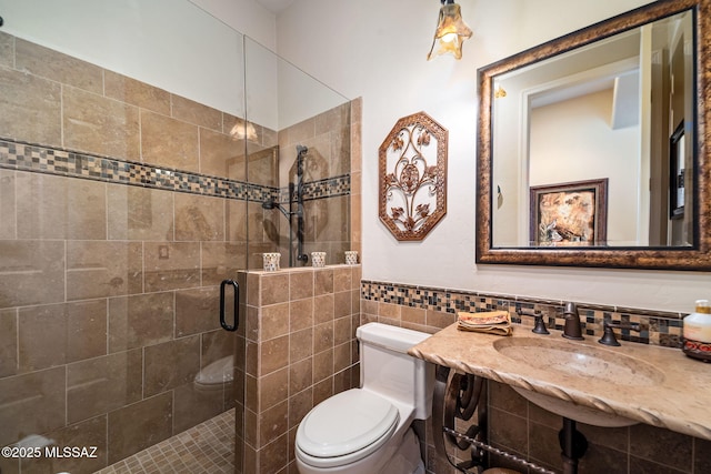 bathroom featuring toilet, a wainscoted wall, a shower stall, and tile walls