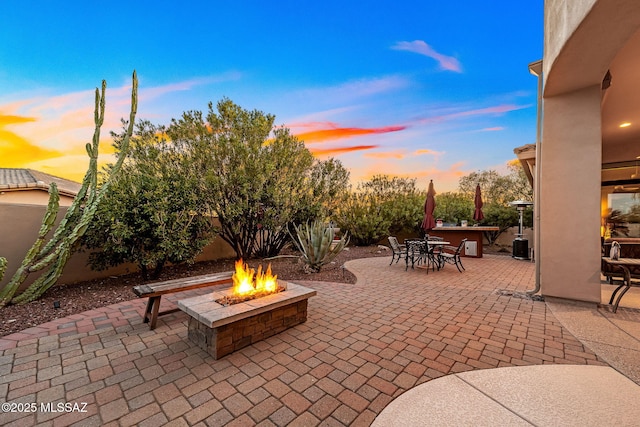 patio terrace at dusk with an outdoor fire pit, fence, and outdoor dining area