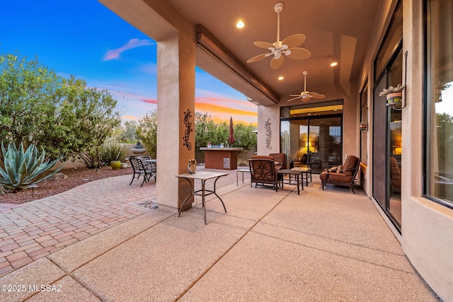 patio terrace at dusk featuring ceiling fan, outdoor dining area, and outdoor lounge area