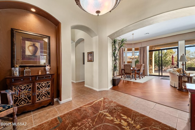 hall featuring baseboards, arched walkways, a notable chandelier, and tile patterned floors