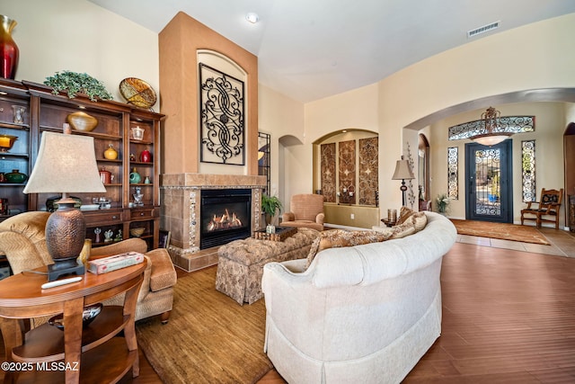 living room featuring arched walkways, a tiled fireplace, wood finished floors, and visible vents