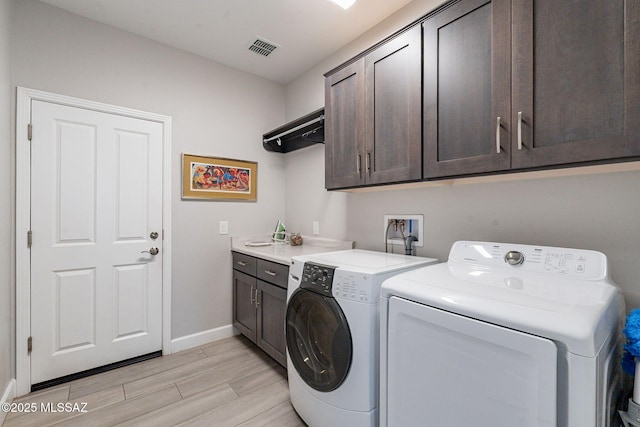 clothes washing area with washing machine and dryer, cabinets, and light wood-type flooring