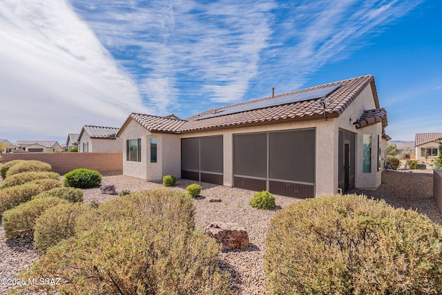 back of property featuring a sunroom and solar panels