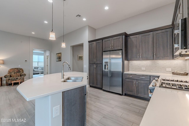 kitchen featuring appliances with stainless steel finishes, decorative light fixtures, sink, backsplash, and a kitchen island with sink