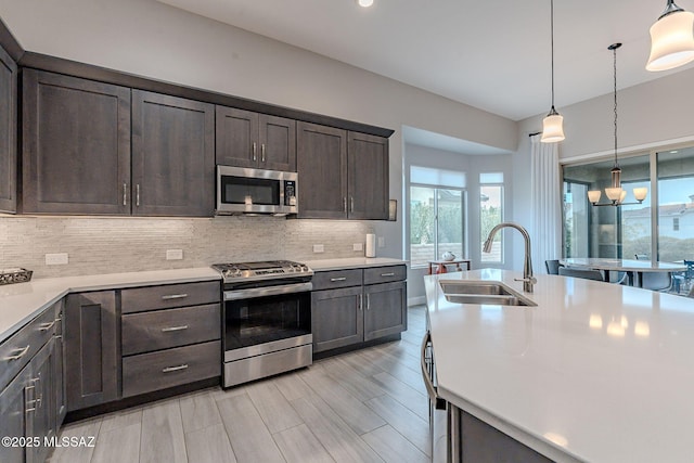 kitchen featuring appliances with stainless steel finishes, sink, dark brown cabinets, and decorative light fixtures