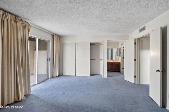 unfurnished bedroom with ensuite bath, carpet flooring, and a textured ceiling