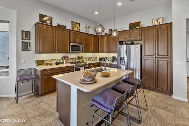 kitchen featuring sink, appliances with stainless steel finishes, a kitchen breakfast bar, a center island with sink, and decorative light fixtures