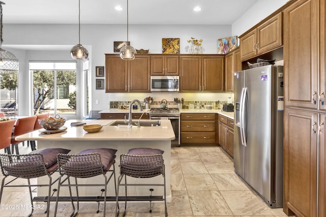 kitchen with pendant lighting, sink, stainless steel appliances, and an island with sink