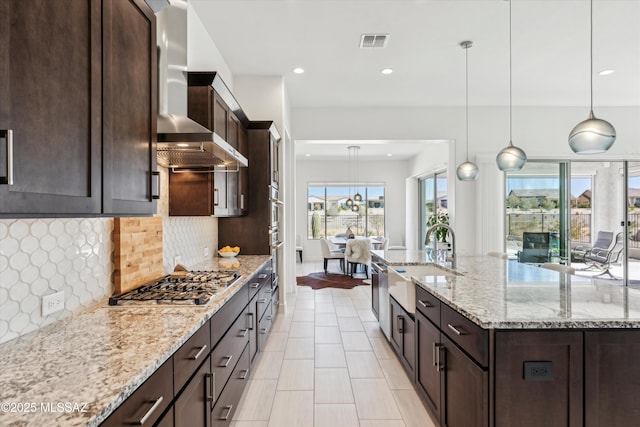 kitchen with hanging light fixtures, light stone countertops, sink, and stainless steel gas stovetop