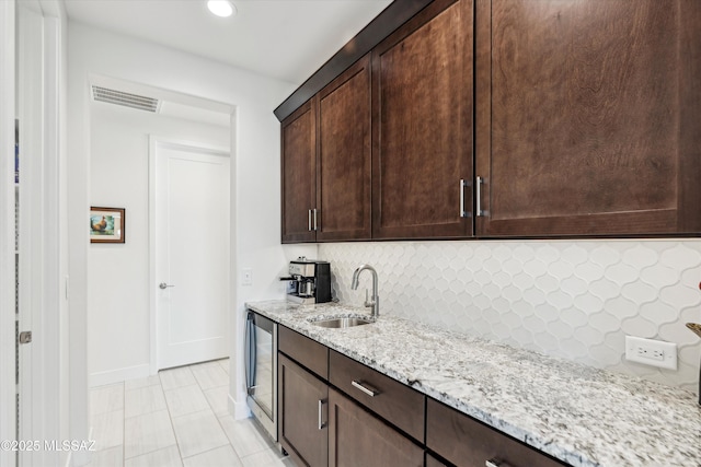 kitchen featuring light tile patterned flooring, sink, tasteful backsplash, dark brown cabinets, and light stone countertops