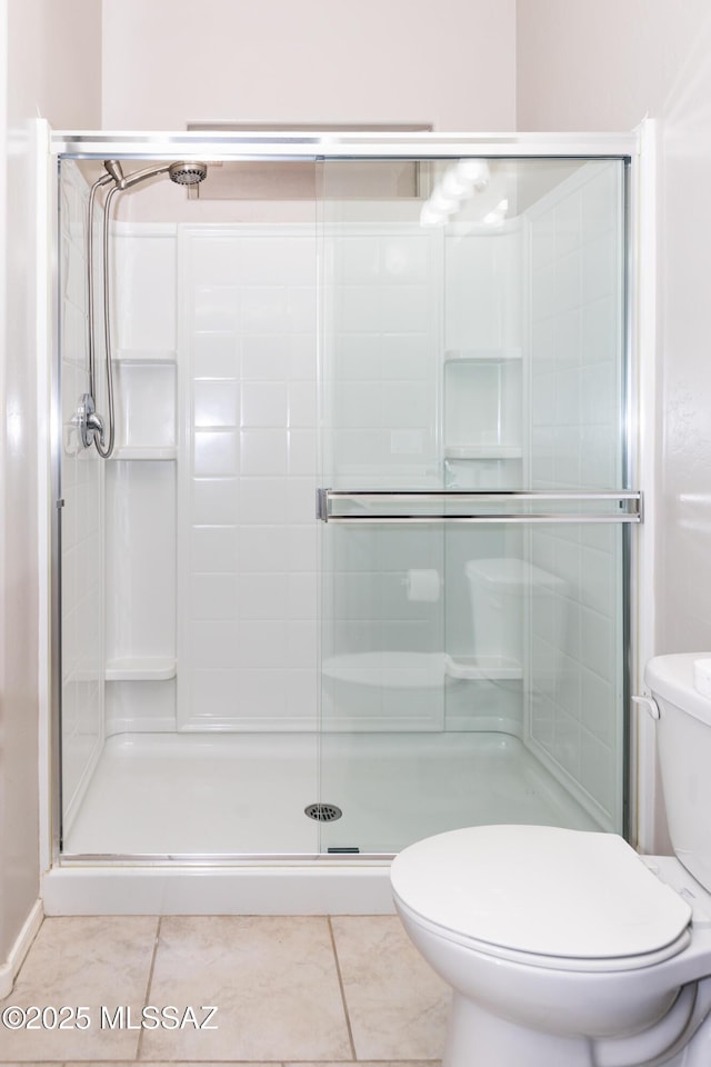 bathroom with tile patterned floors, toilet, and a shower with door