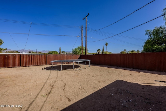 view of yard featuring a trampoline, a fenced backyard, and a mountain view