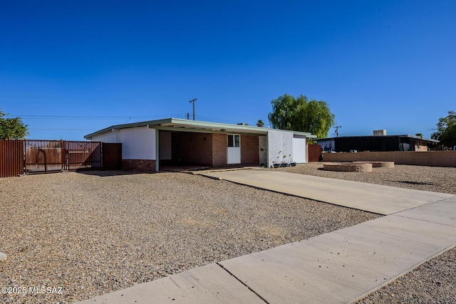 view of front facade featuring driveway, an attached carport, fence, and brick siding