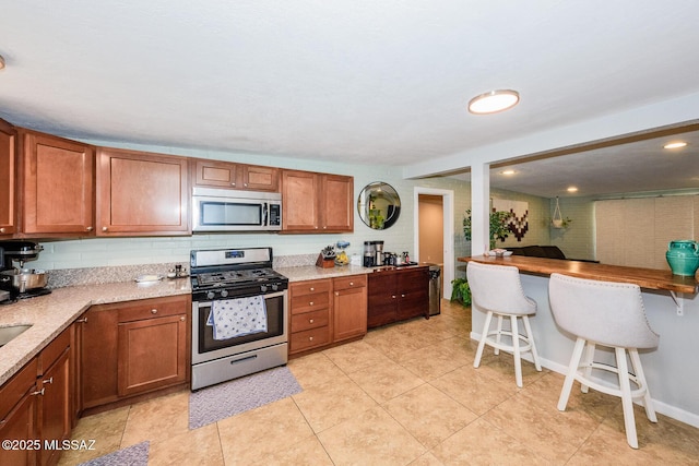 kitchen featuring brown cabinets, light tile patterned floors, stainless steel appliances, and backsplash