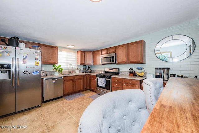 kitchen with appliances with stainless steel finishes, brown cabinets, a sink, and light tile patterned flooring