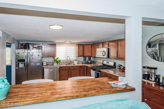 kitchen featuring stainless steel appliances, backsplash, a sink, and brown cabinets