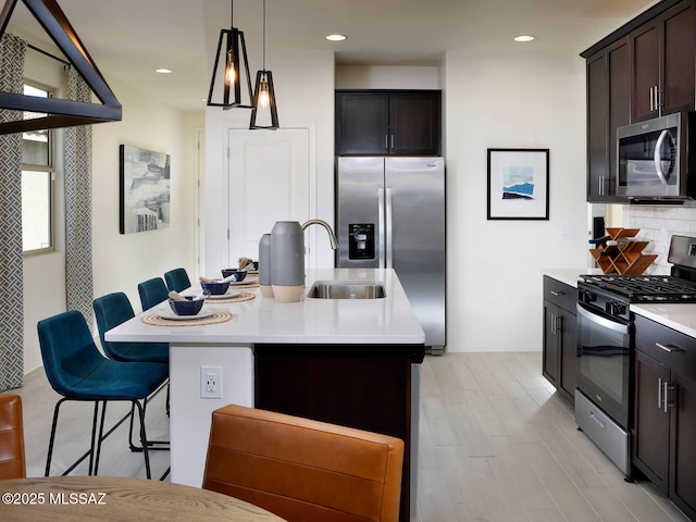 kitchen with pendant lighting, a breakfast bar, a kitchen island with sink, stainless steel appliances, and dark brown cabinetry