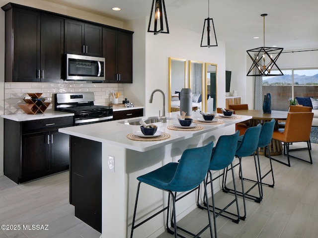 kitchen featuring sink, a breakfast bar area, hanging light fixtures, stainless steel appliances, and a center island with sink