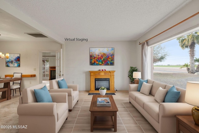 living room with visible vents, a notable chandelier, a glass covered fireplace, and a textured ceiling
