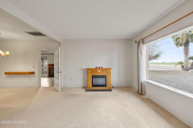 unfurnished living room featuring a textured ceiling, a glass covered fireplace, visible vents, carpet floors, and a chandelier