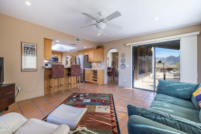 living area with light tile patterned floors, visible vents, arched walkways, and a ceiling fan