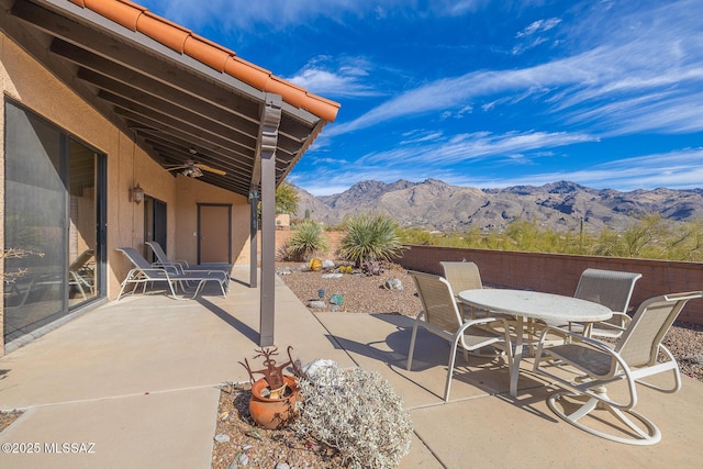 view of patio / terrace with fence, a mountain view, a ceiling fan, and outdoor dining space