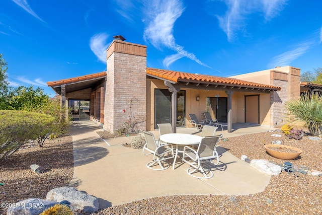 rear view of property with a patio area, a tile roof, a chimney, and stucco siding